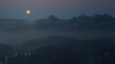 黄昏时分，宁静的月光笼罩着雪山和森林，薄雾弥漫，气氛安谧