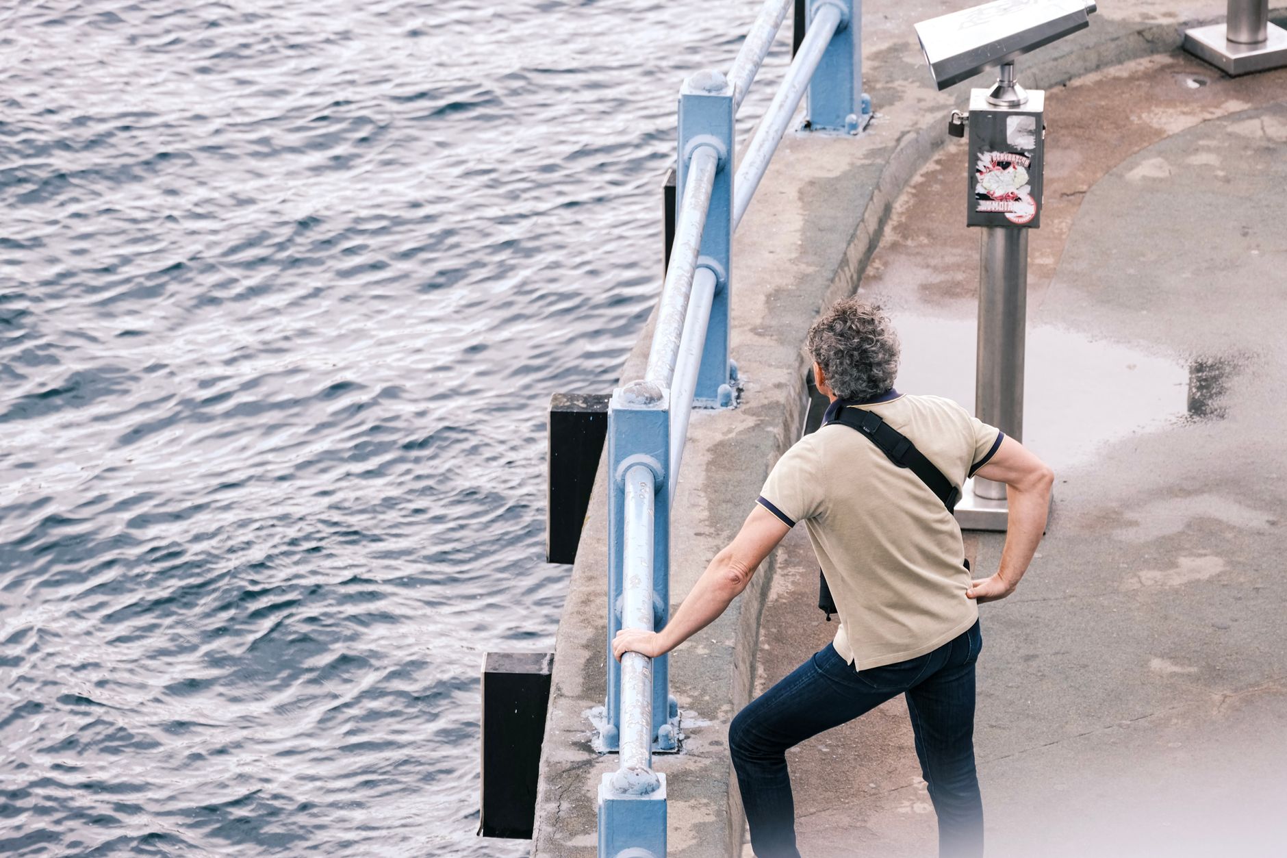 A man stands by the ocean railing at a coastal viewpoint, observing the sea.
