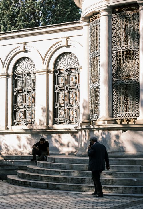 Free Ornate building facade with intricate ironwork, two people on steps; city urban scene. Stock Photo
