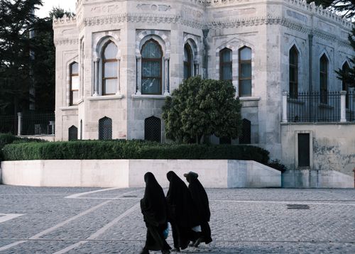 Free Three individuals in traditional attire walking by historic building. Stock Photo