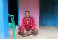 Senior woman in traditional attire sitting outside a colorful house.