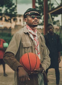 A stylish young man with sunglasses holds a basketball outdoors, exuding confidence and style.