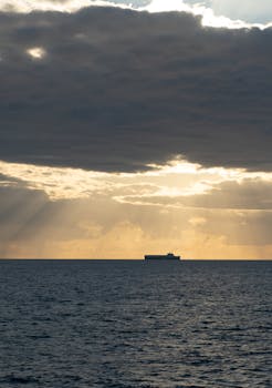 一艘货船在大洋上航行，其背后是令人惊叹的日落景象，而前方则形成了引人注目的云层