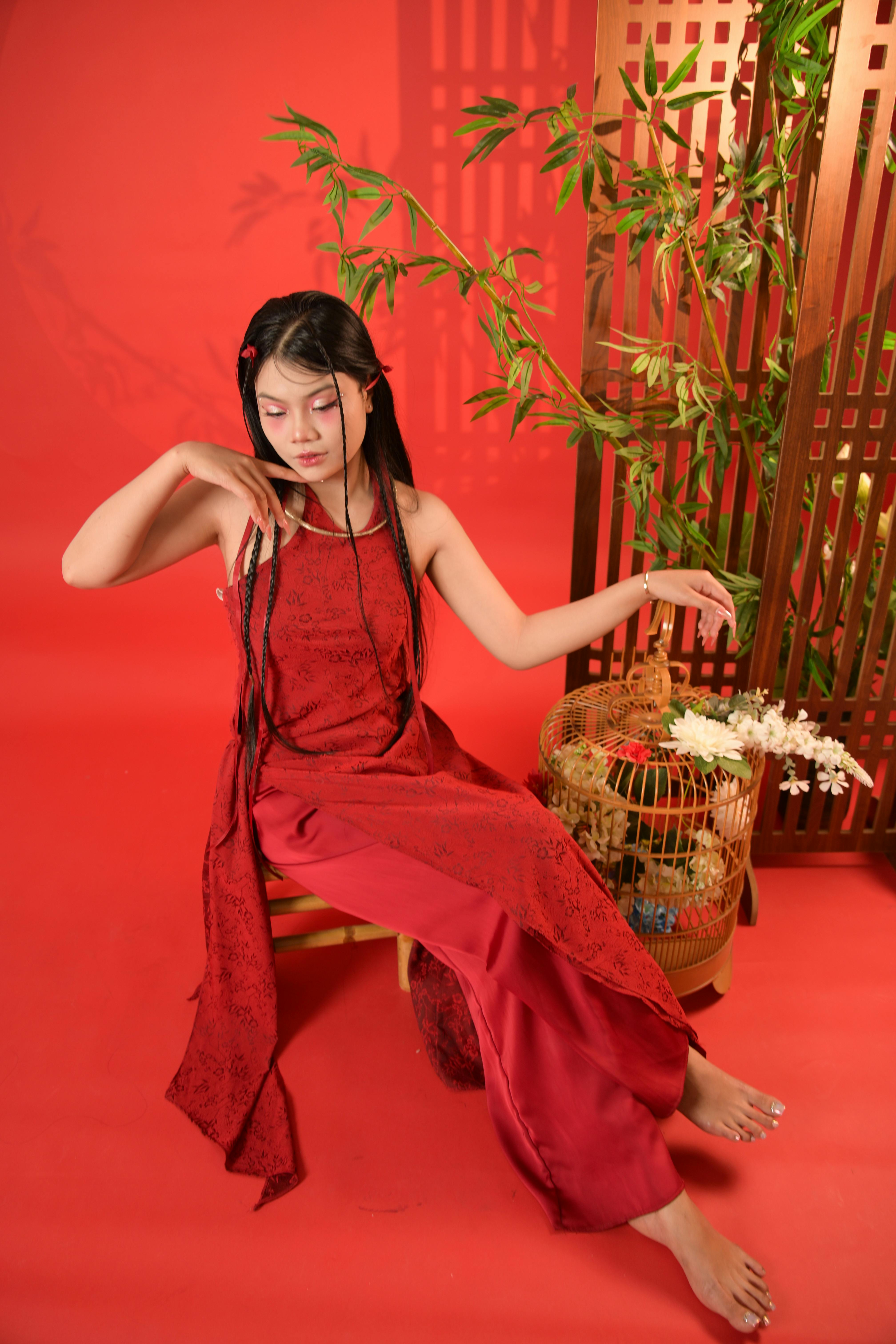 Woman in a traditional red dress poses gracefully indoors near bamboo decor.