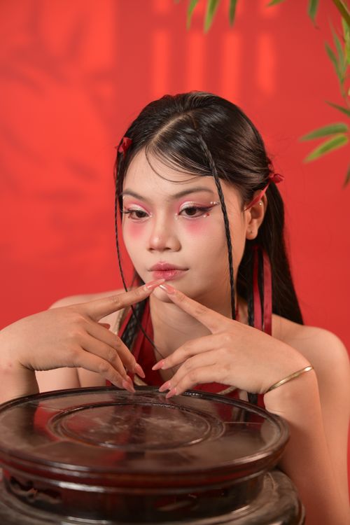 Free Portrait of an Asian woman with striking makeup against a vibrant red background. Stock Photo