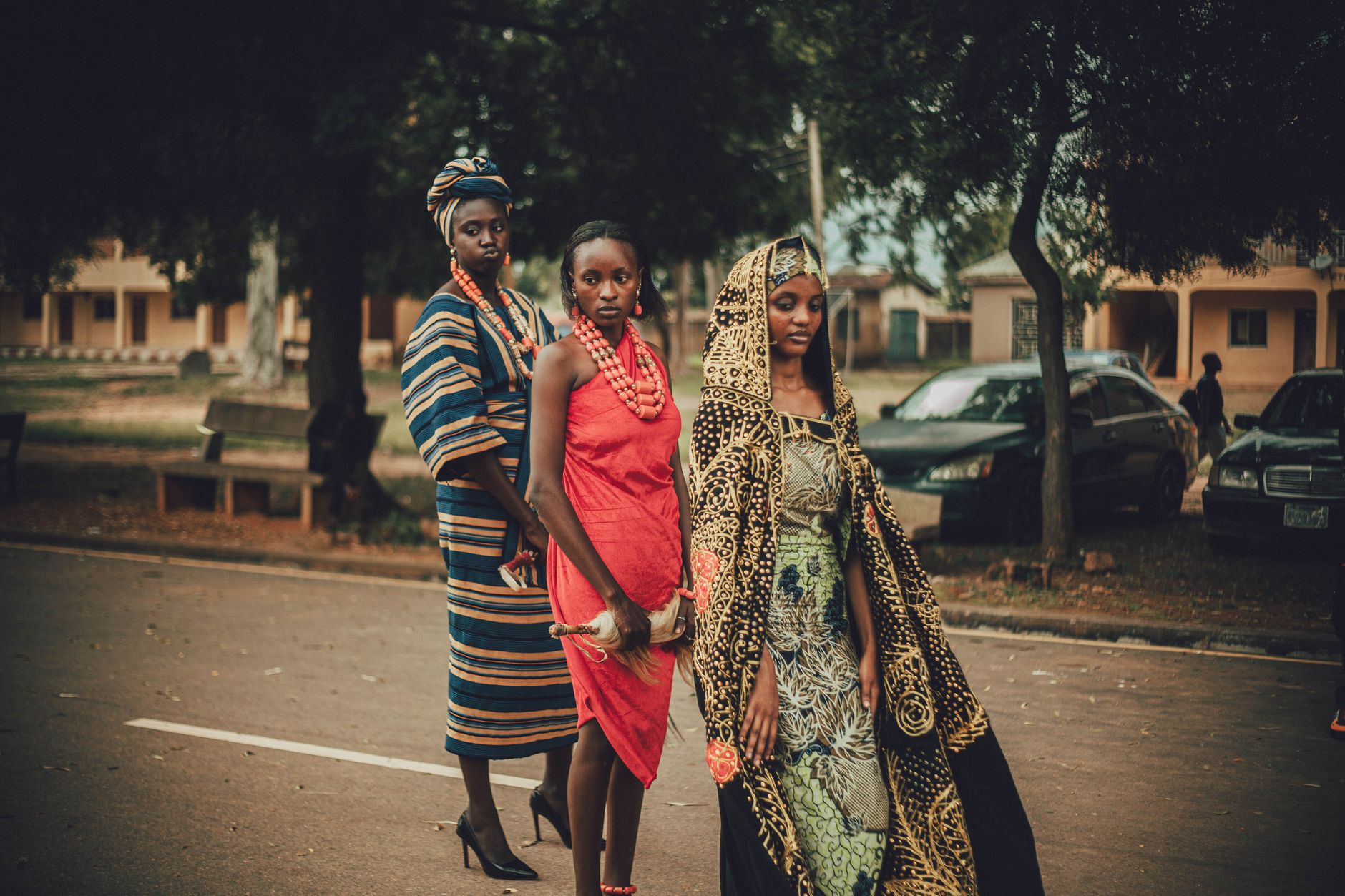 Three women showcasing traditional African attire in a street scene, emphasizing cultural heritage.