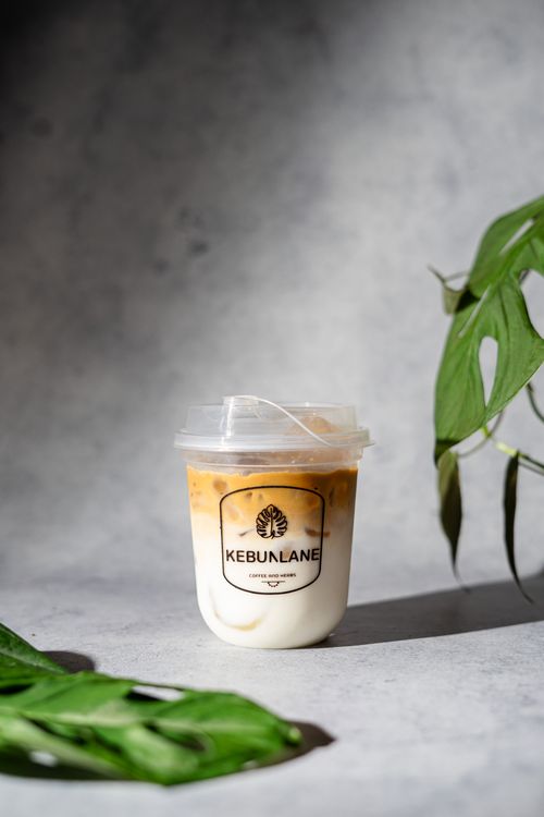 Free A refreshing iced coffee with milk in a branded cup alongside green leaves on a gray background. Stock Photo