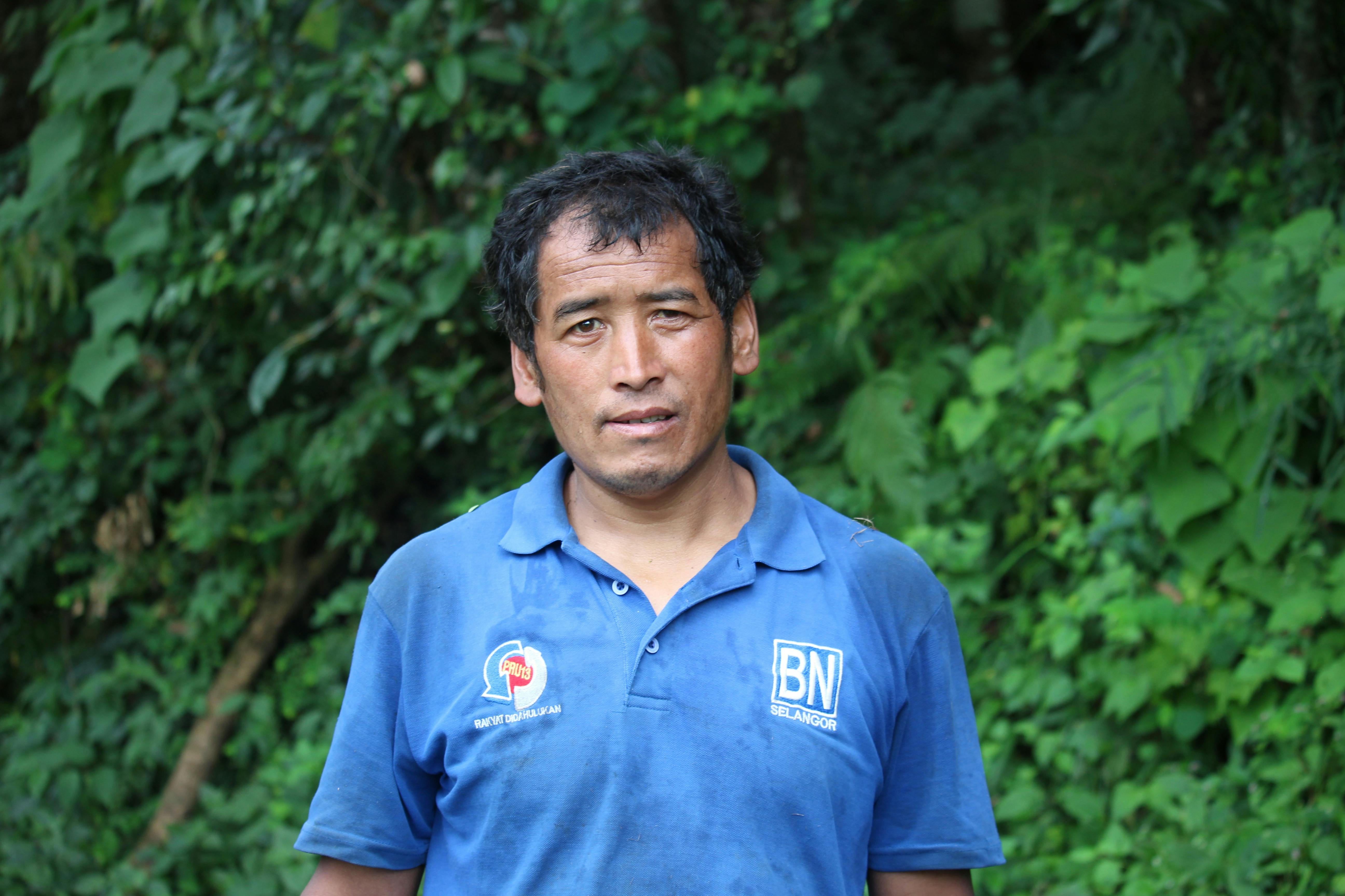 A man standing outdoors in the greenery of a Nepali village.