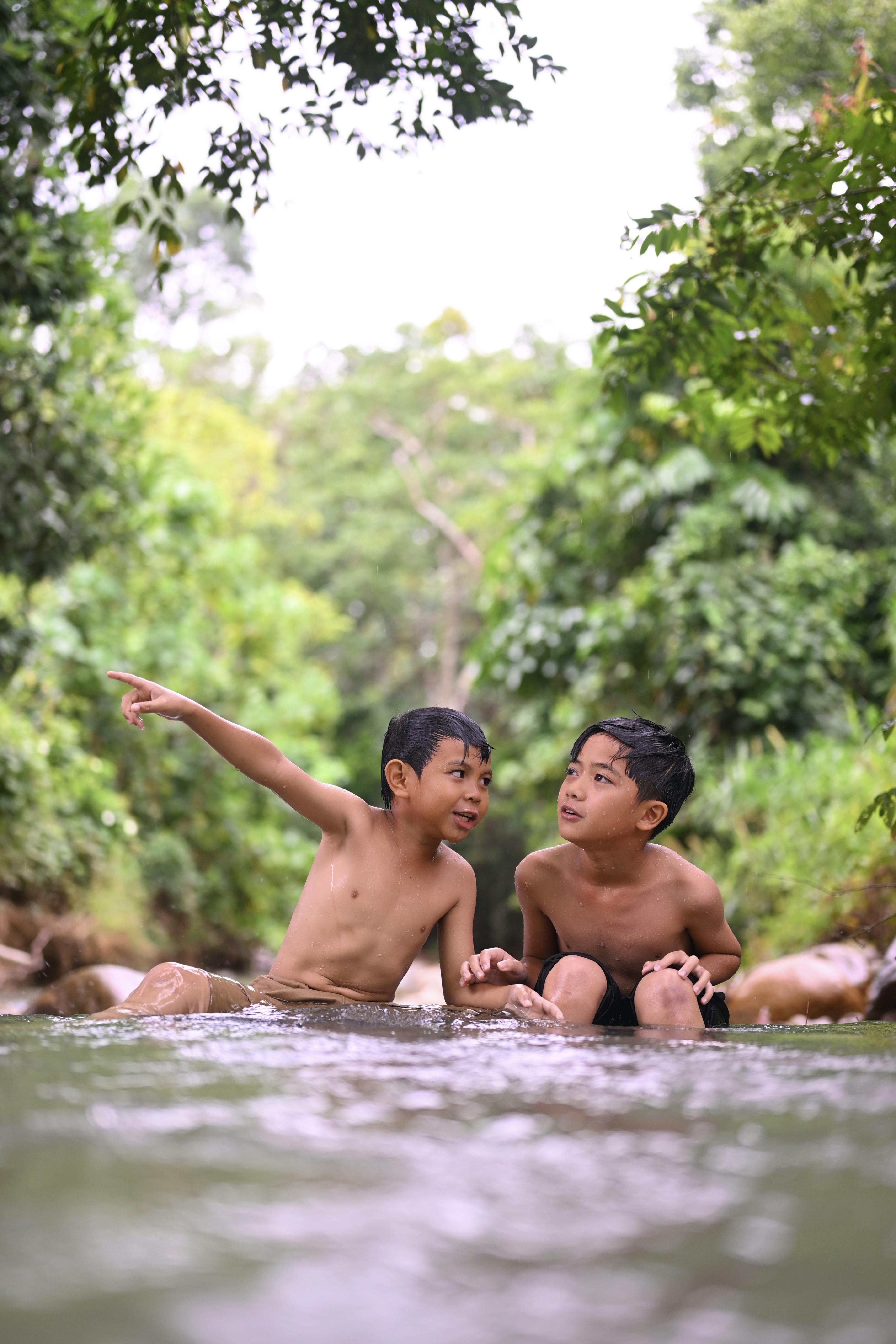 Two children play joyfully in a tropical stream surrounded by lush greenery in Sabah, Malaysia.
