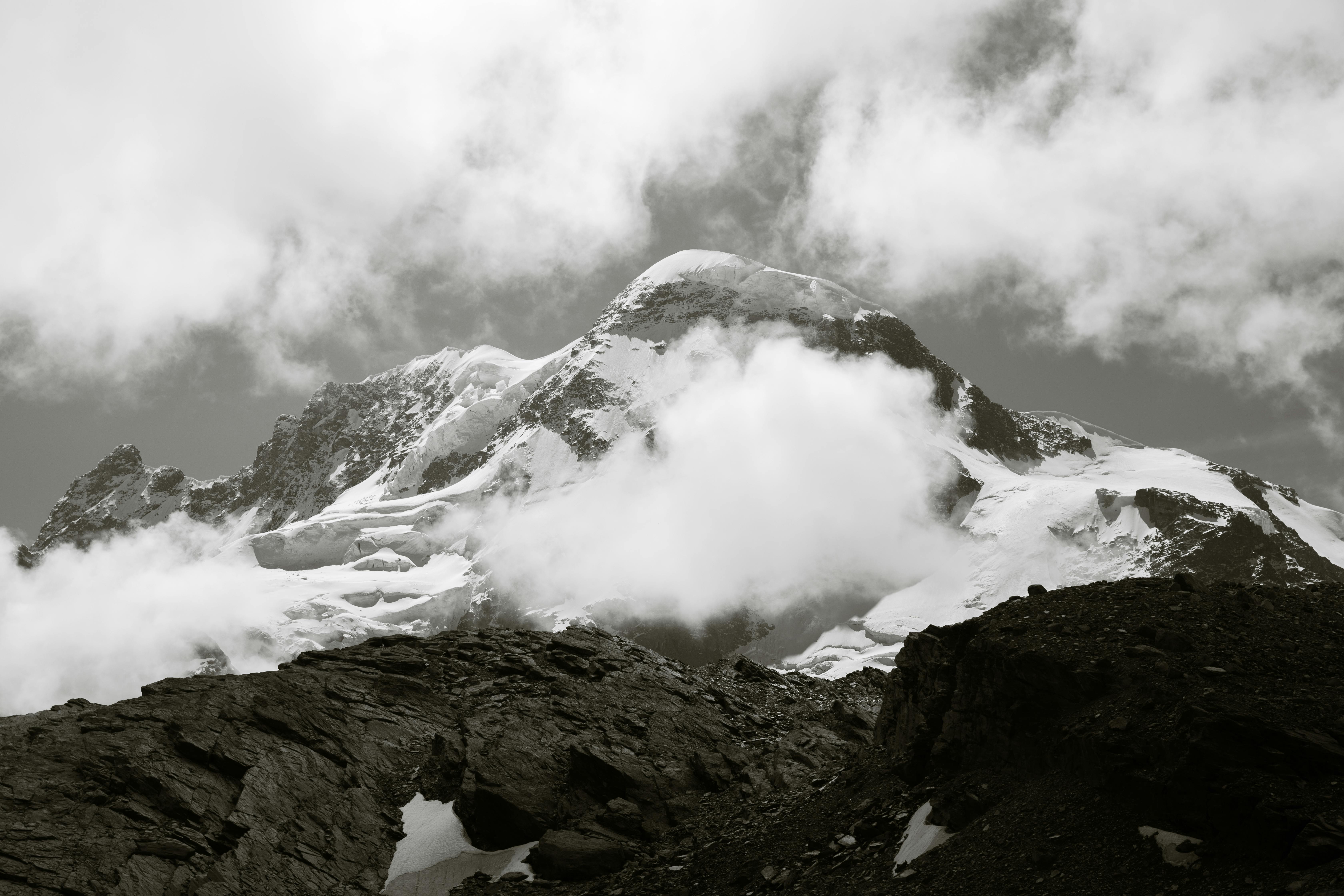 Breathtaking black and white photo of snow-covered peaks and clouds in Zermatt, capturing nature's raw beauty.