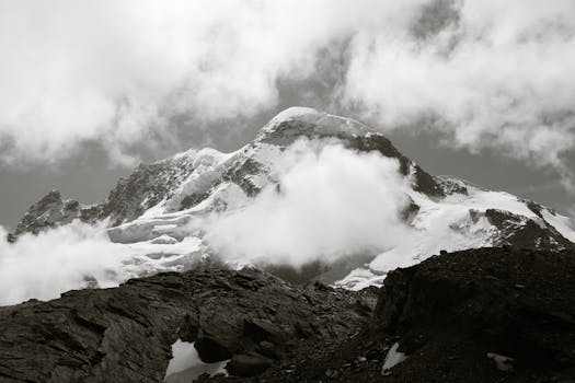 Breathtaking black and white photo of snow-covered peaks and clouds in Zermatt, capturing nature's raw beauty.