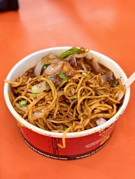 Delicious spicy Hakka noodles in a disposable container, perfect for takeout or street food dining.