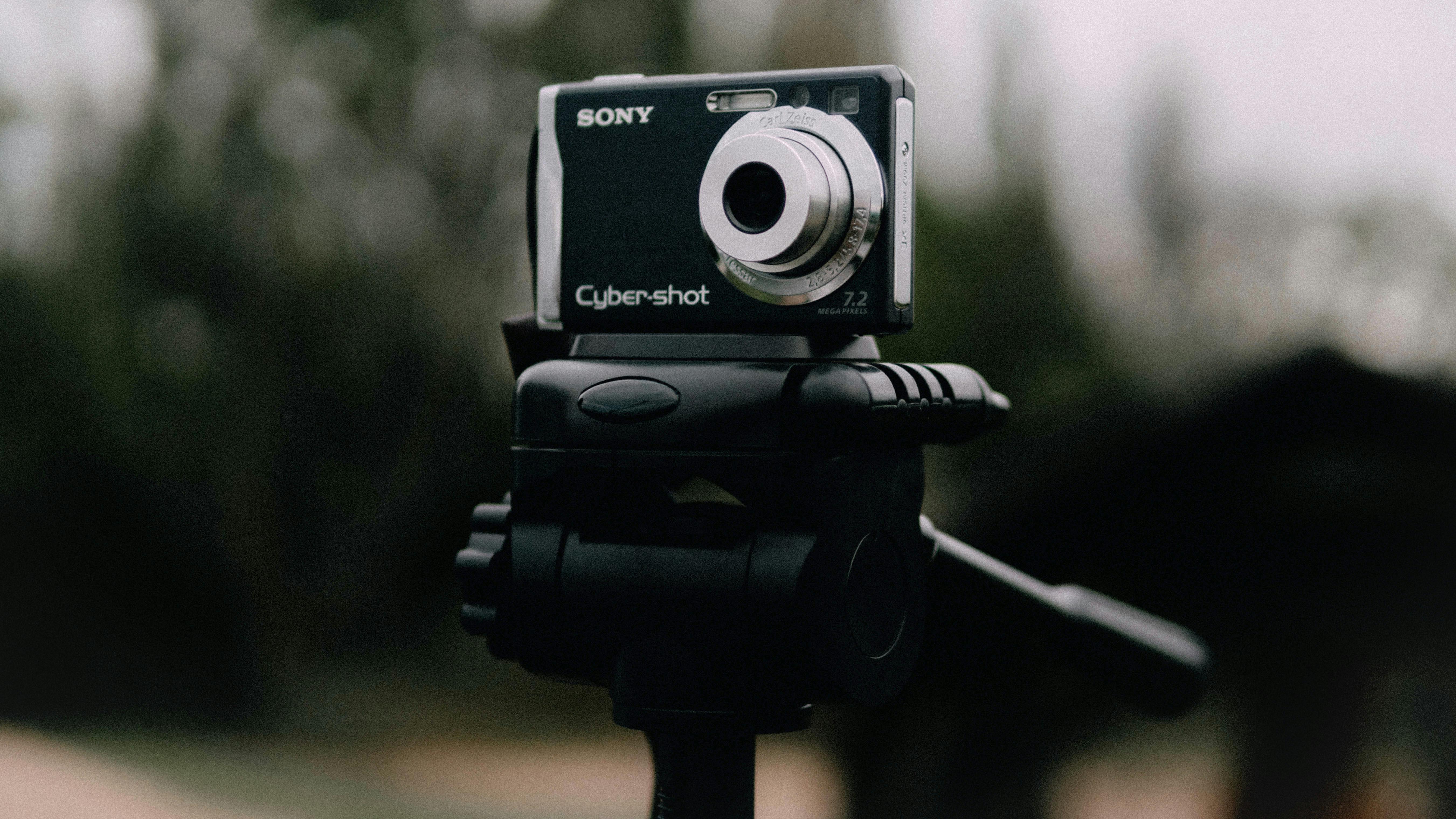 Gratis Una macchina fotografica digitale montata su un treppiede all'aperto con uno sfondo sfocato. Foto a disposizione