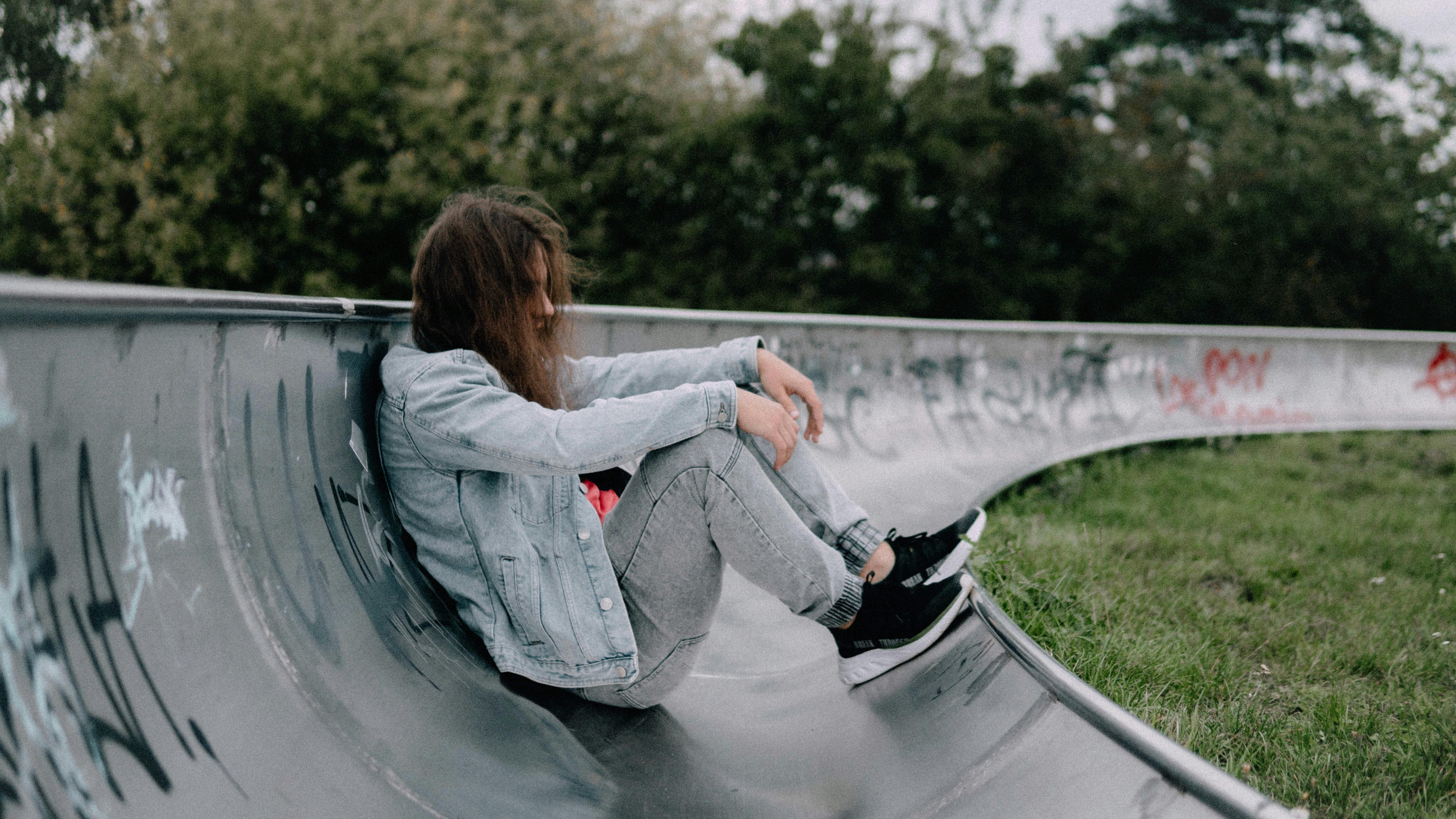 Gratis Ung voksen sittende i en skatepark med graffiti, som fremkaller en avslappet og urban atmosfære. Arkivbilde