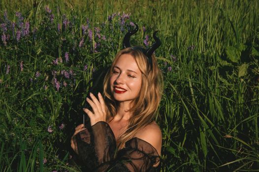 Young woman with devil horns smiling in a lush green field under the sun.
