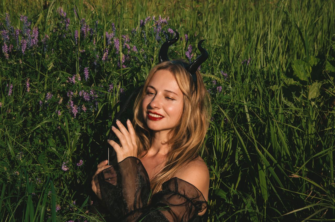 young woman with devil horns smiling in a lush green field under the s