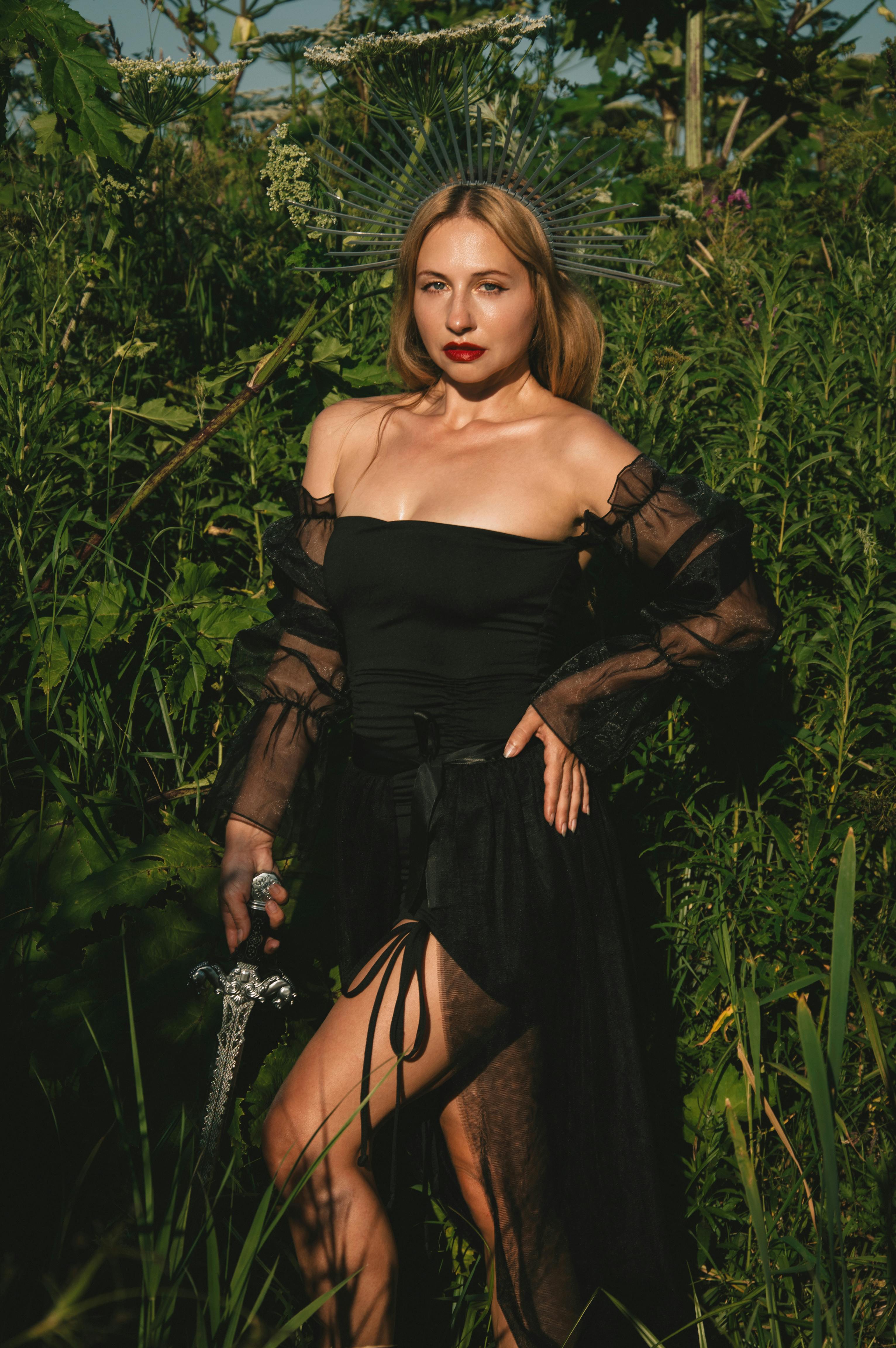 一个女人穿着黑色礼服，站在郁郁葱葱的绿色背景前，头饰精美