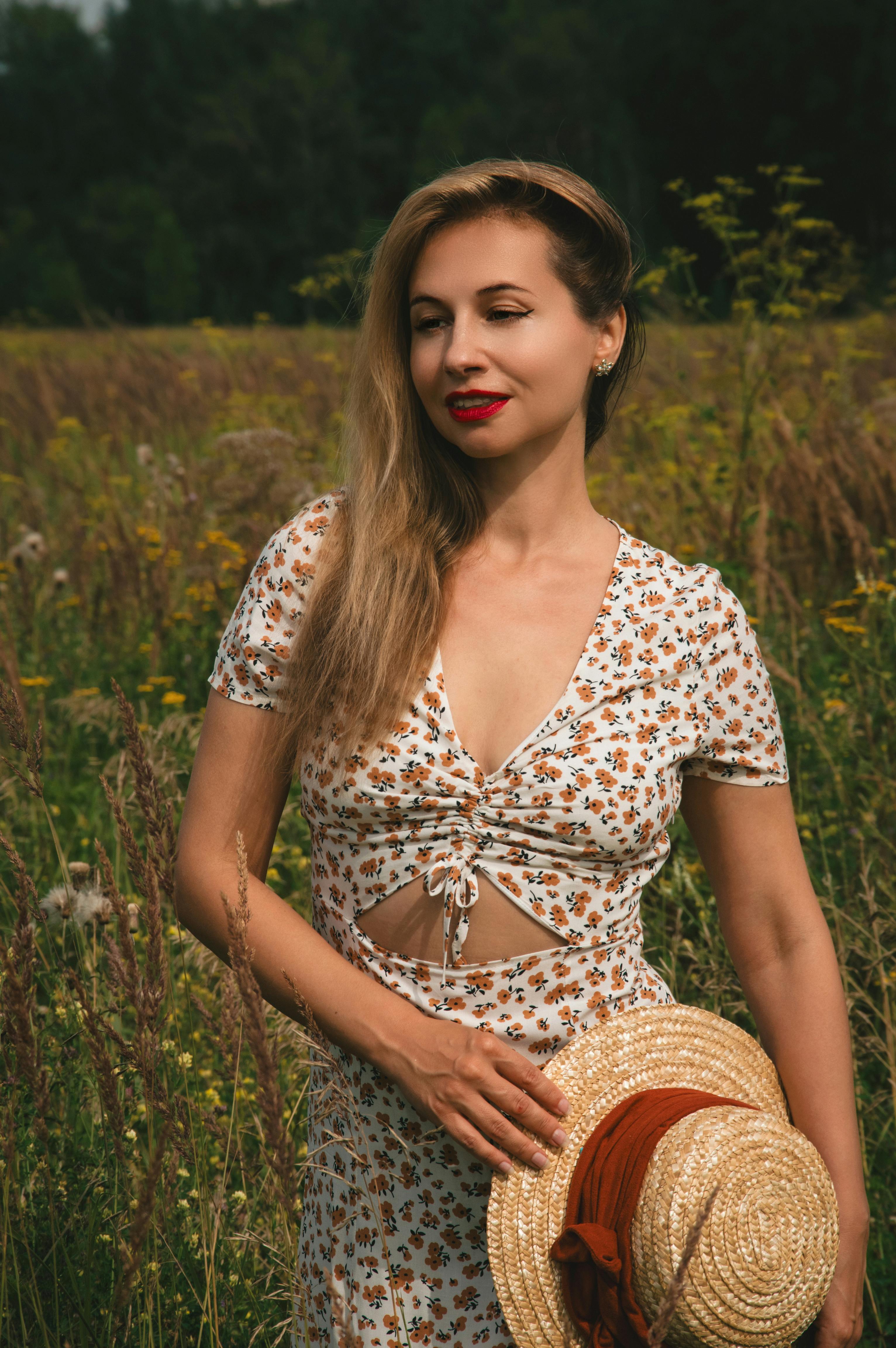 一个穿着花裙子的女人站在阳光明媚的草地上，手里拿着草帽