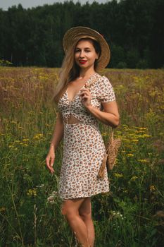 Woman in a floral summer dress and straw hat standing in a wildflower meadow.
