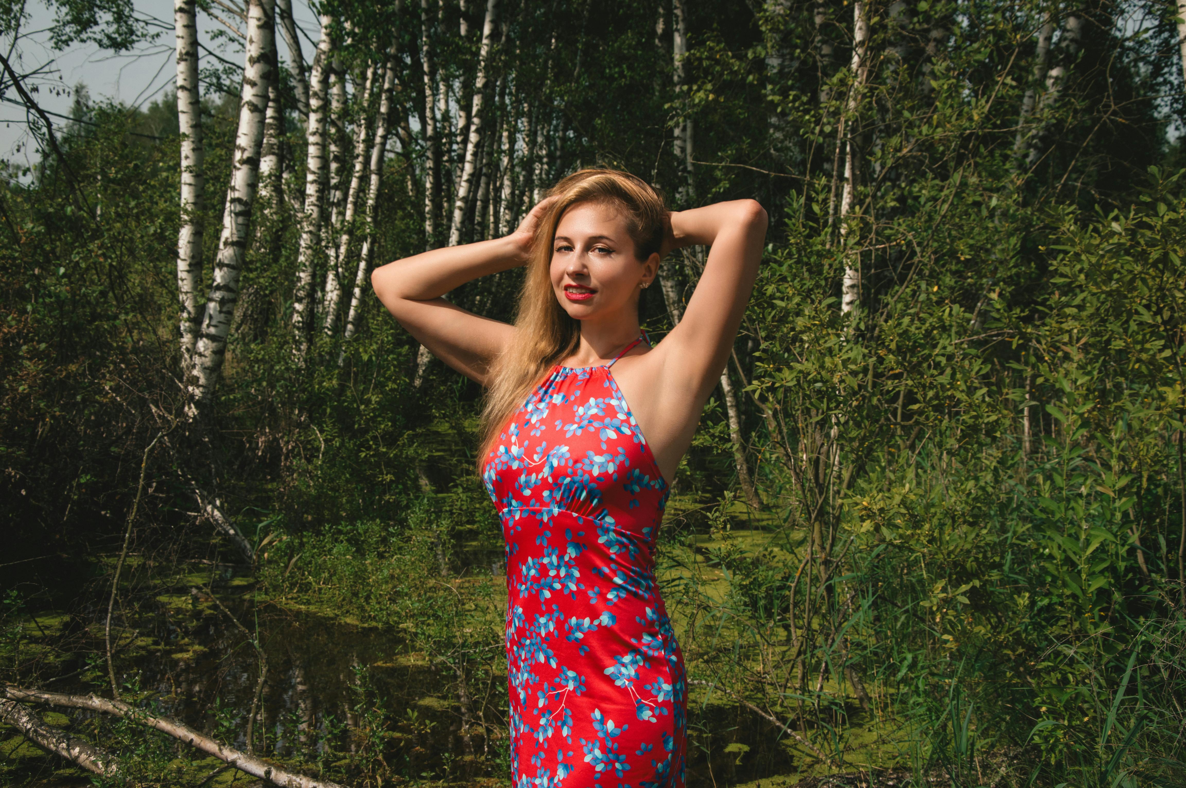 一名身穿红色花卉连衣裙的女子在郁郁葱葱的森林中自信地摆姿势