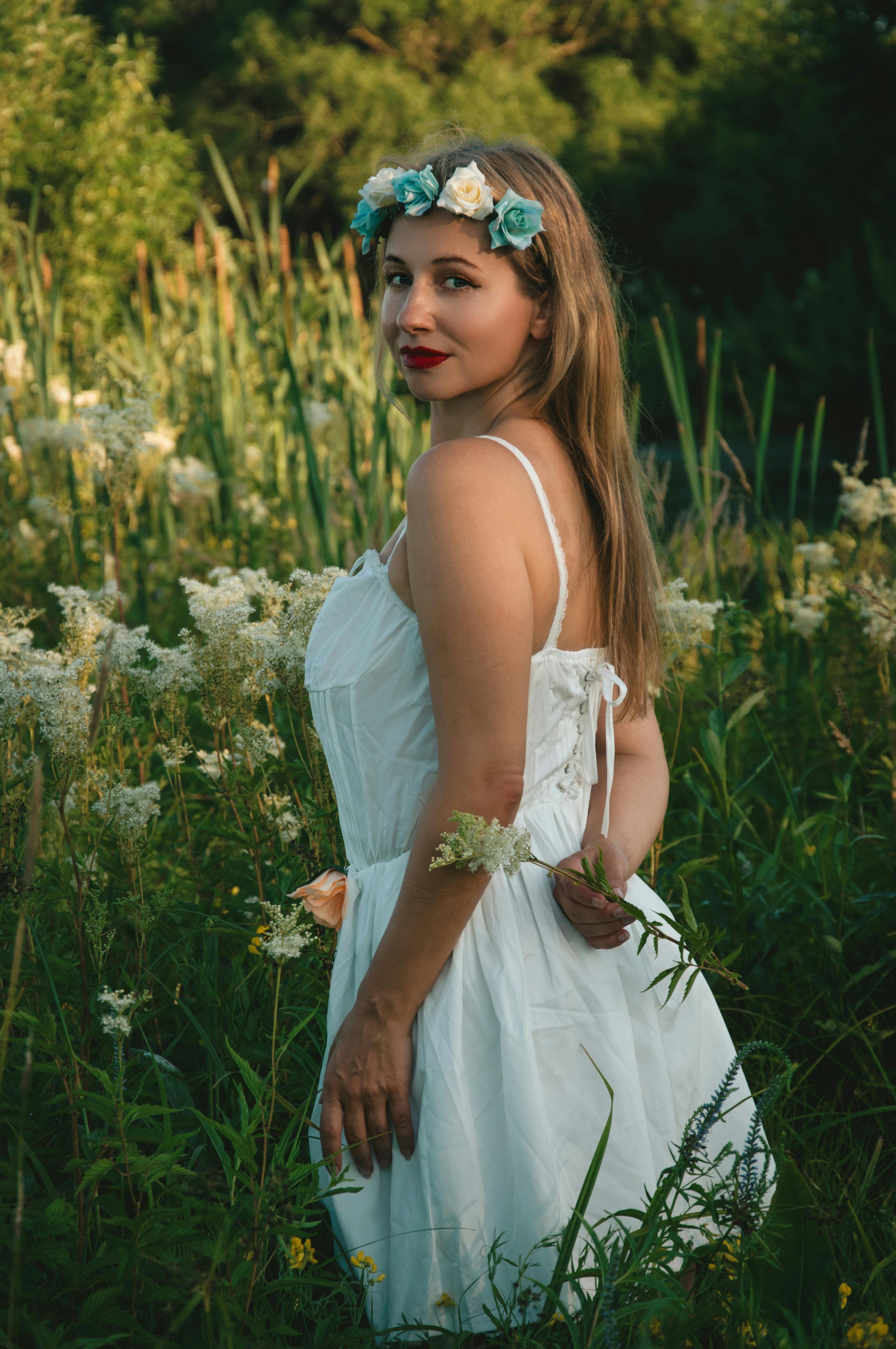 头戴花卉王冠的女子站在郁郁葱葱的绿色草地上，身着白色连衣裙