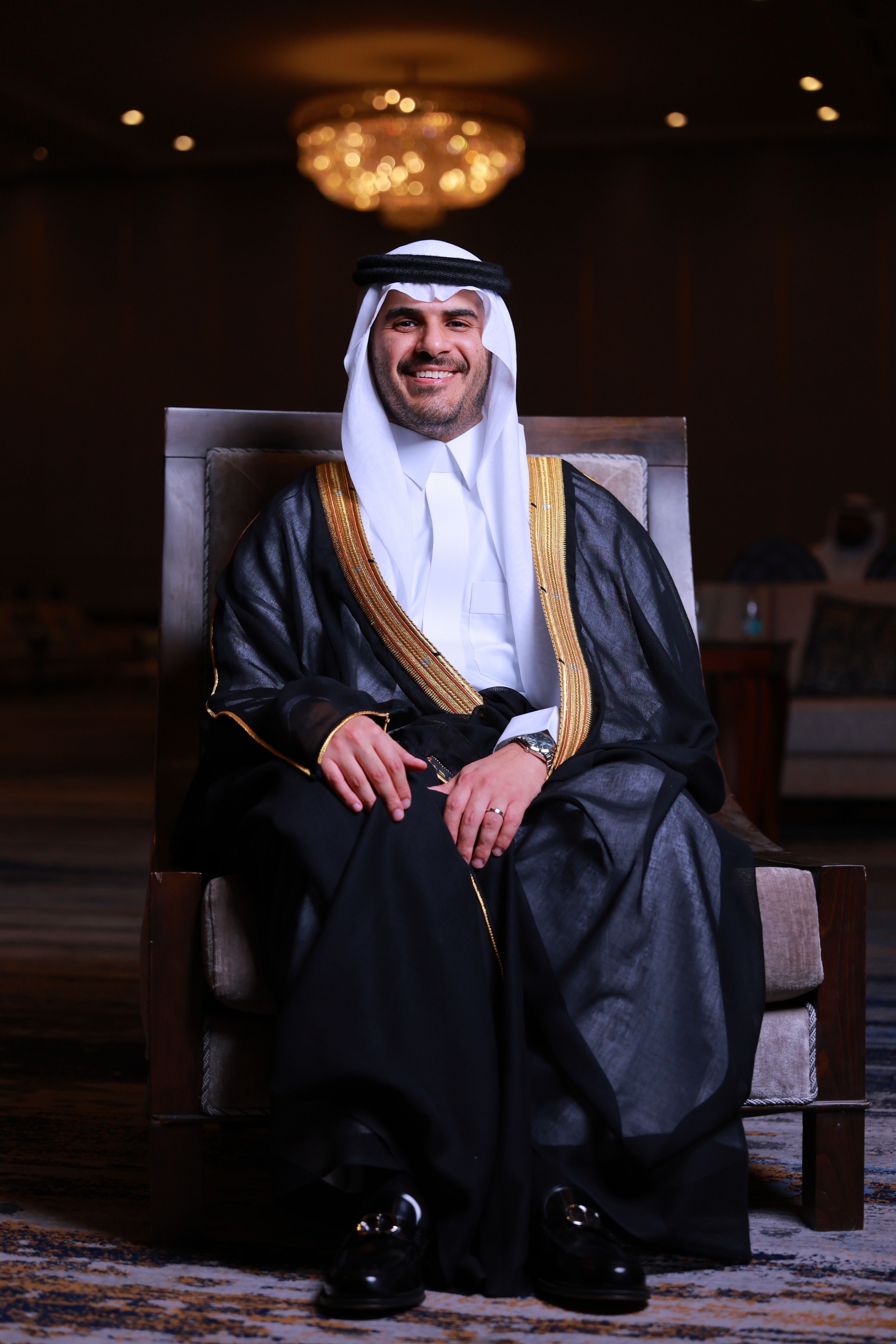 Portrait of a smiling man wearing traditional Middle Eastern attire seated indoors.