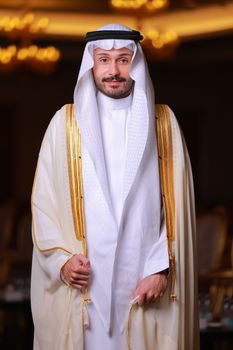 Man wearing traditional Middle Eastern clothing standing indoors with elegant lighting.