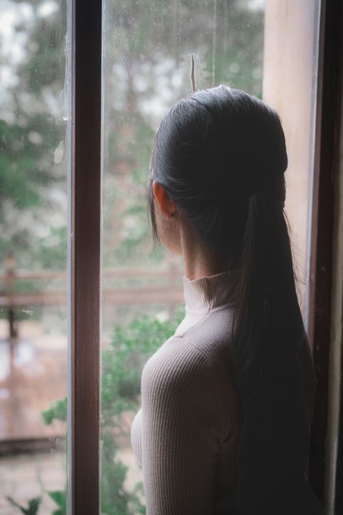Free A serene woman with long hair looks out a window, contemplating nature. Stock Photo