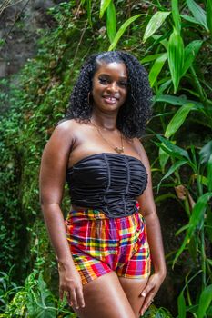 Smiling woman stands outdoors among lush greenery, exuding vibrant summer vibes.
