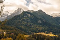在多云的天空下，高山山脉、郁郁葱葱的森林以及白雪皑皑的山峰构成了一幅令人惊叹的画面