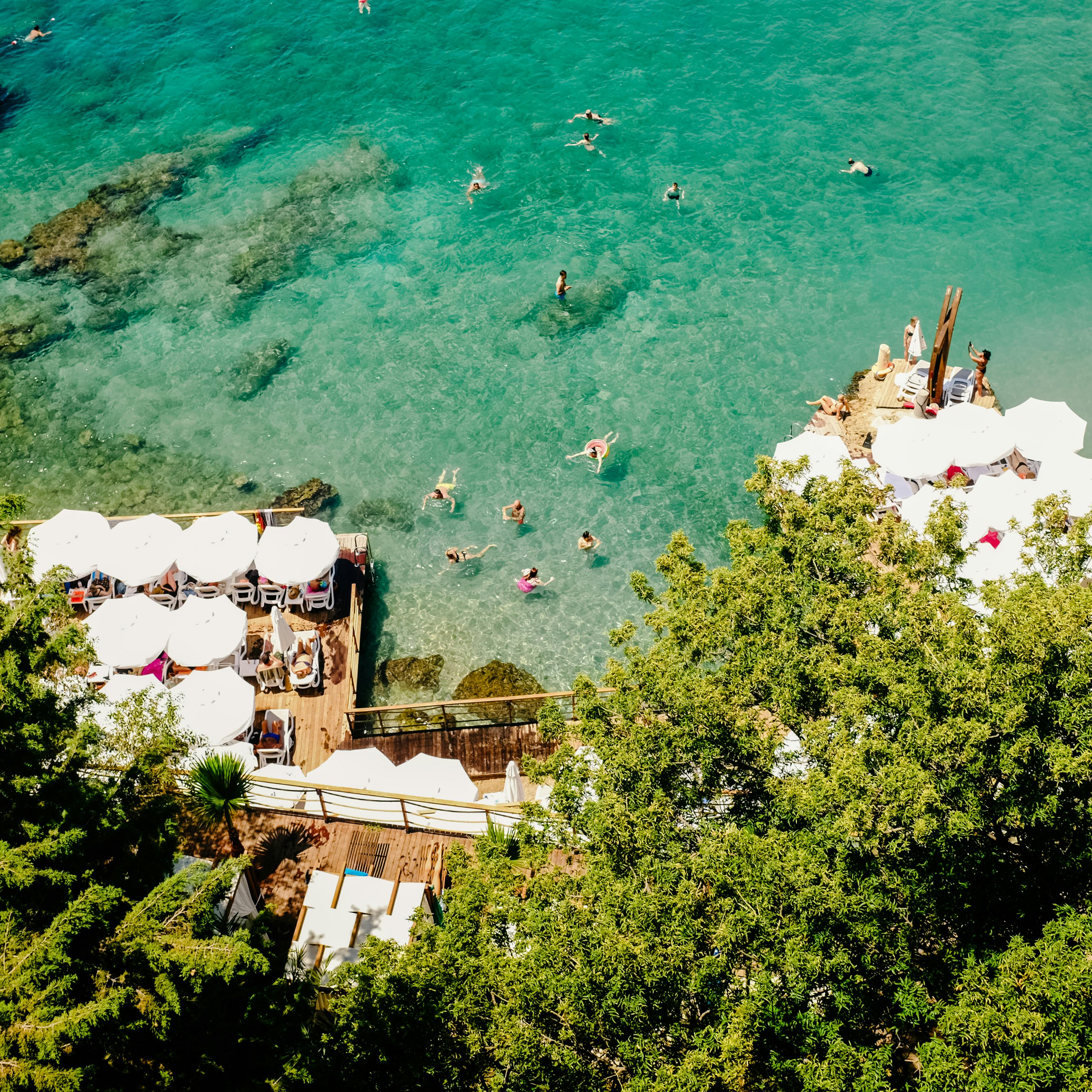 充满活力的海滩场景在空中拍摄中得以呈现，游泳者和日光浴者在清澈的蓝色大海和晴朗天气中尽情享受