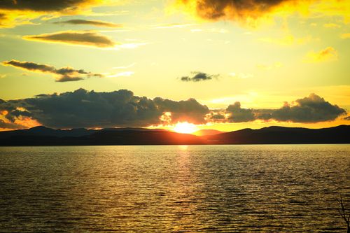 Free Capture of a breathtaking sunset over a calm ocean, silhouetted by distant mountains and clouds. Stock Photo