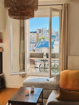 Bright and cozy living room with an open window view of city rooftops, perfect for urban lifestyle inspiration.