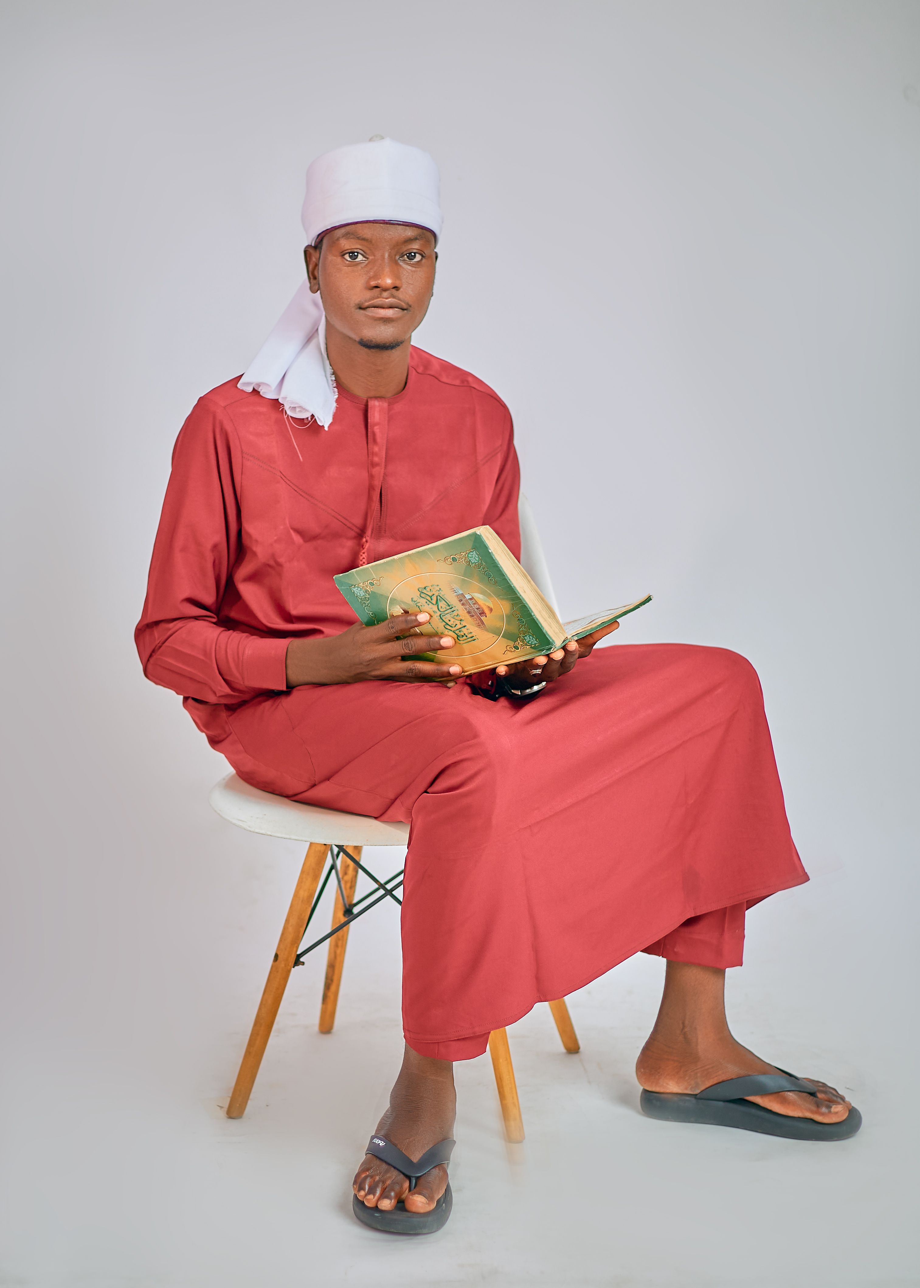 Young man seated, reading a religious book, dressed in traditional attire.