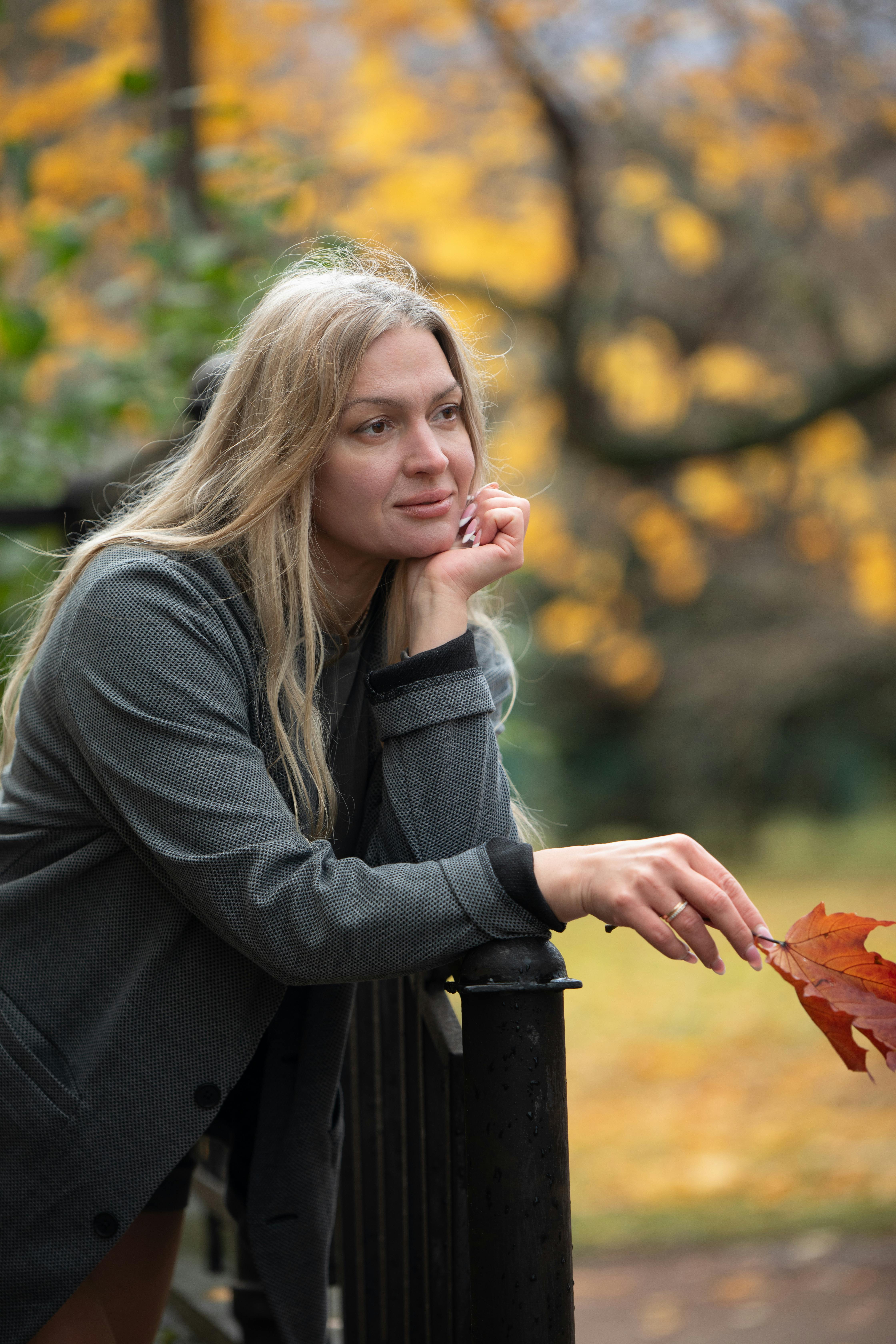 一位体贴的女人靠在栏杆上，周围的秋叶生机勃勃，营造出宁静的景象