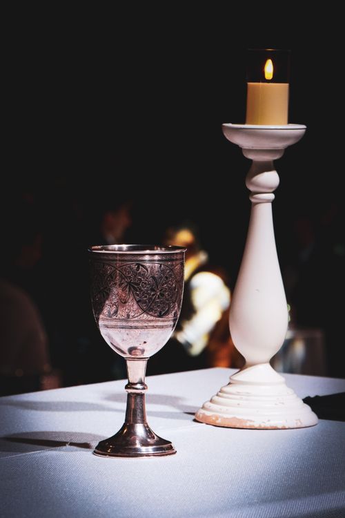 Free Intricate silver chalice and lit candle on table in warm, moody light. Stock Photo