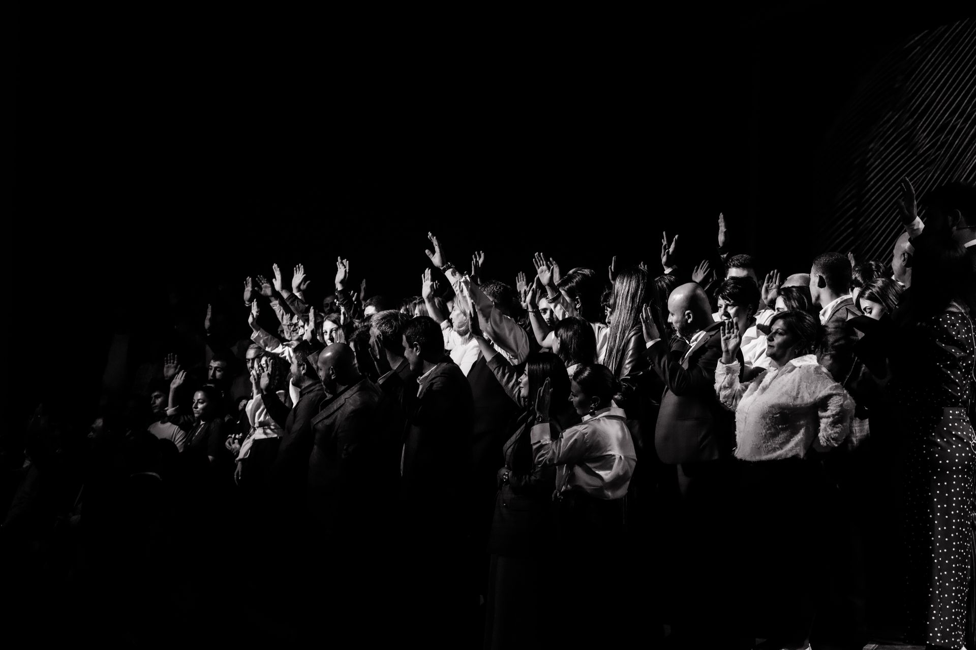 A dynamic black and white scene of a crowded group raising hands in unison at an event.