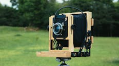 郁郁葱葱的绿色户外环境中，一台经典木制野外相机安装在三脚架上