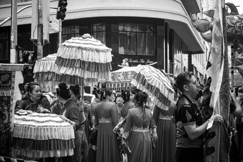 Free Black and white street scene of a cultural parade with decorative umbrellas and participants in traditional attire. Stock Photo
