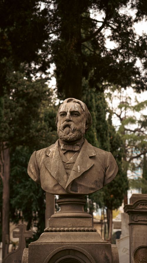 Free Stone bust of a historic figure in a serene cemetery, surrounded by trees. Stock Photo