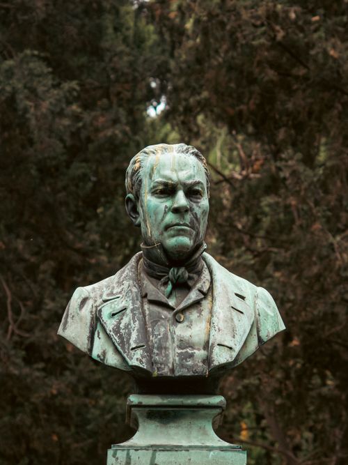 Free Bronze bust of a historical figure in a serene outdoor setting. Stock Photo