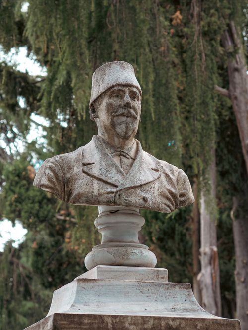 Free A stone bust of a historical figure in an outdoor park setting surrounded by greenery. Stock Photo