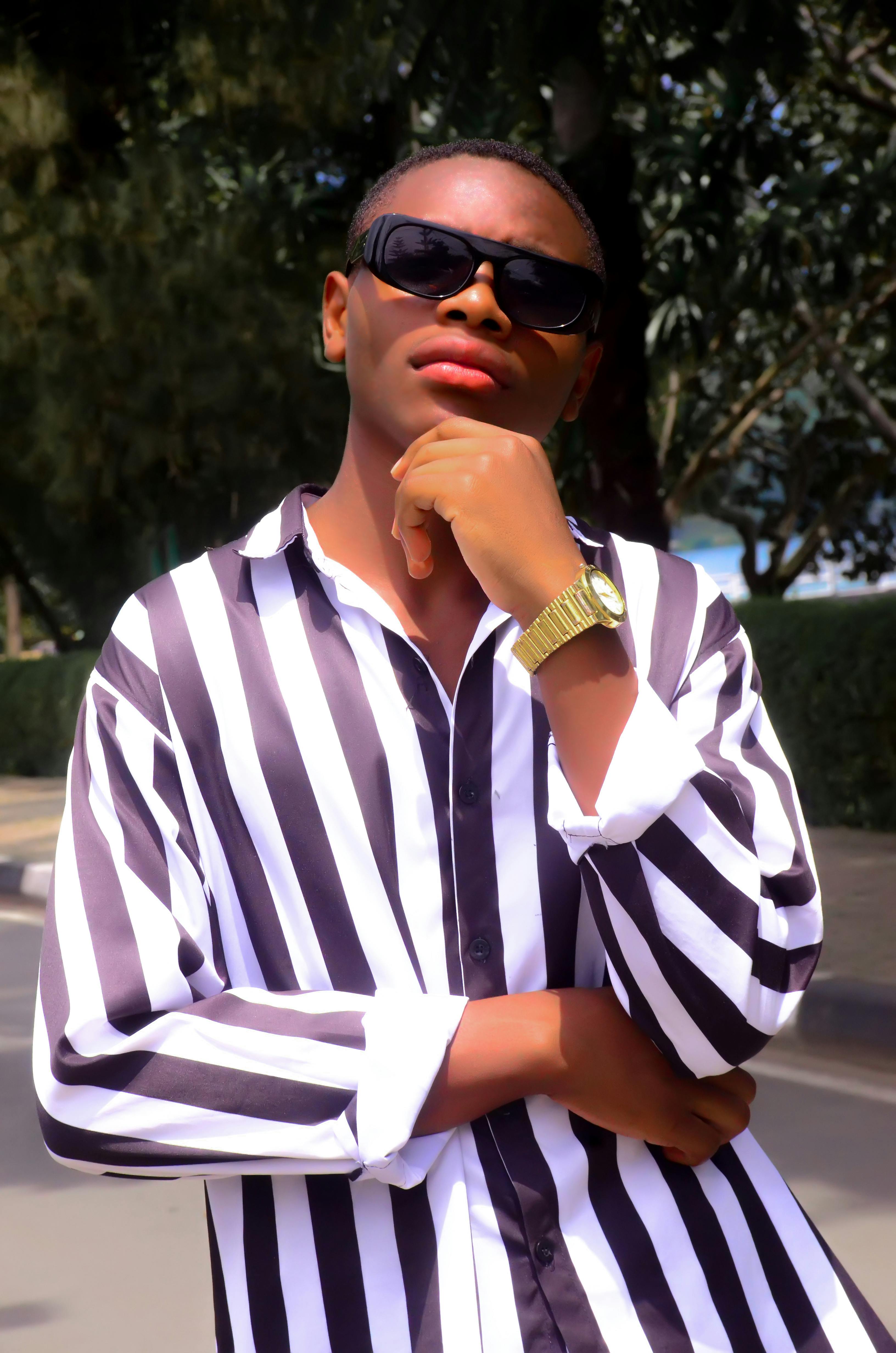 Young man wearing sunglasses and a striped shirt posing confidently outdoors.