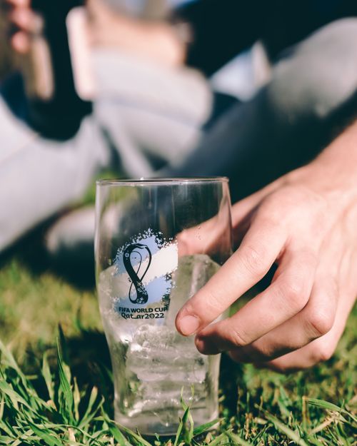 Free Friends enjoying a sunny day outdoors with a FIFA World Cup Qatar 2022 glass. Stock Photo