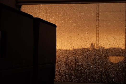 Capture of a moody scene through a rainy train window at sunset.