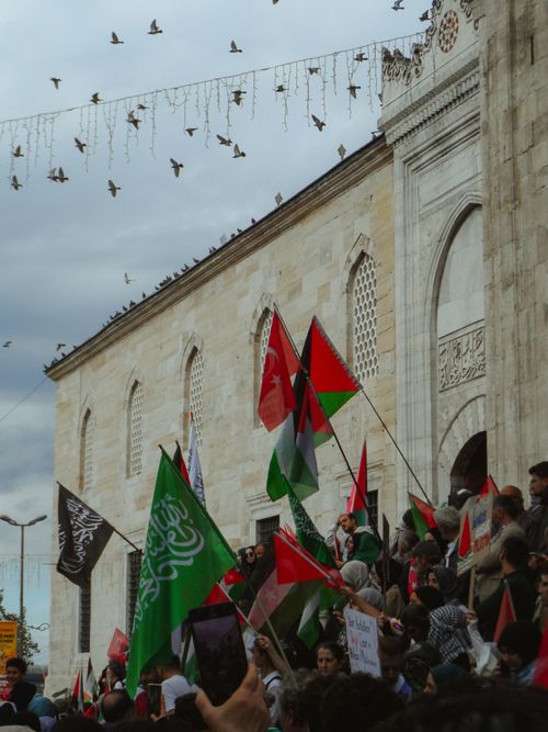 Free Crowd with flags in front of a historic mosque during a lively protest. Stock Photo