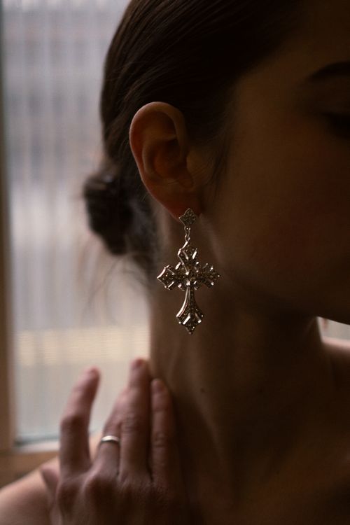 Free Close-up of a woman's profile highlighting a cross-shaped silver earring, captured in soft lighting indoors. Stock Photo