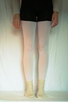 Minimalist aesthetic portrait highlighting fashion in white leggings and socks with a neutral background.