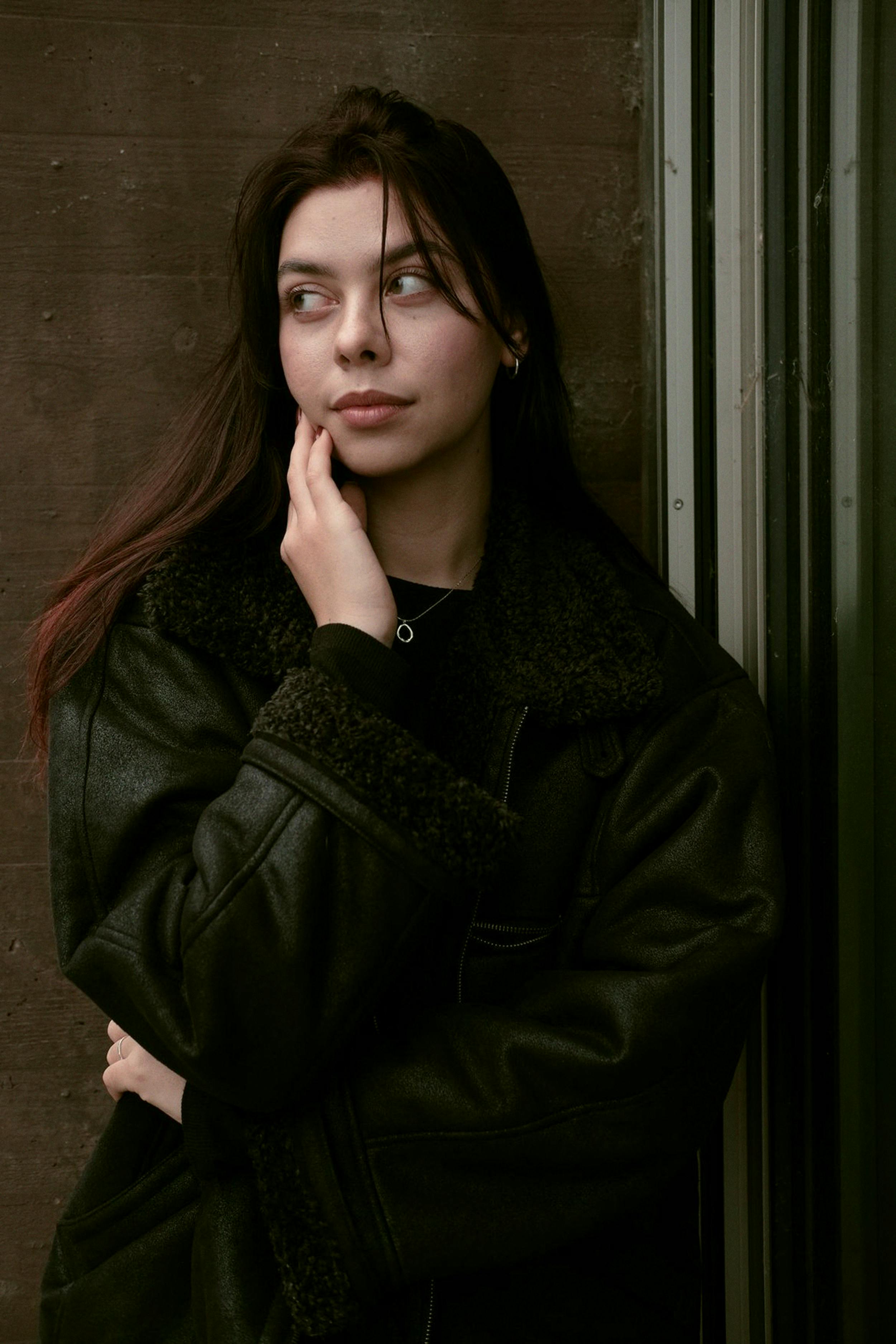 Young woman in a leather jacket gazes thoughtfully, blending style with emotion.
