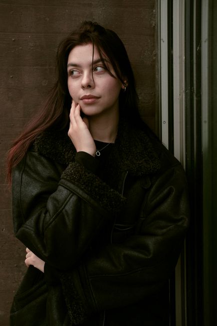 Young woman in a leather jacket gazes thoughtfully, blending style with emotion.